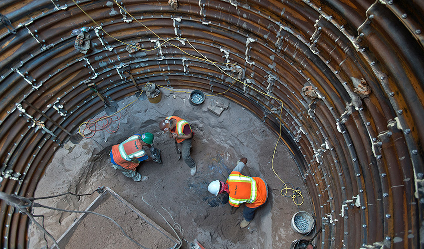 Workers in manhole digging around a steel encased microtunnel. (CC BY 2.0)