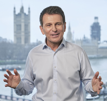 Andre Lacroix, Caucasian man with dark short hair, gesturing with his hands, wearing light-colored button-down shirt.  British Parliament and Big Ben buildings in background