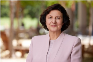 Annamaria Lusardi, woman with short dark hair wearing light pink suit jacket, standing outdoors, with trees in the background
