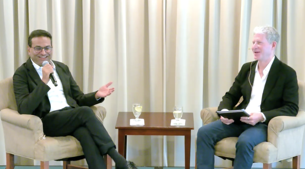 Laxman Narasimhan and Chris Larsen speaking at an event at San Fancisco State University, sitting in two chairs on a stage with a small table between them.